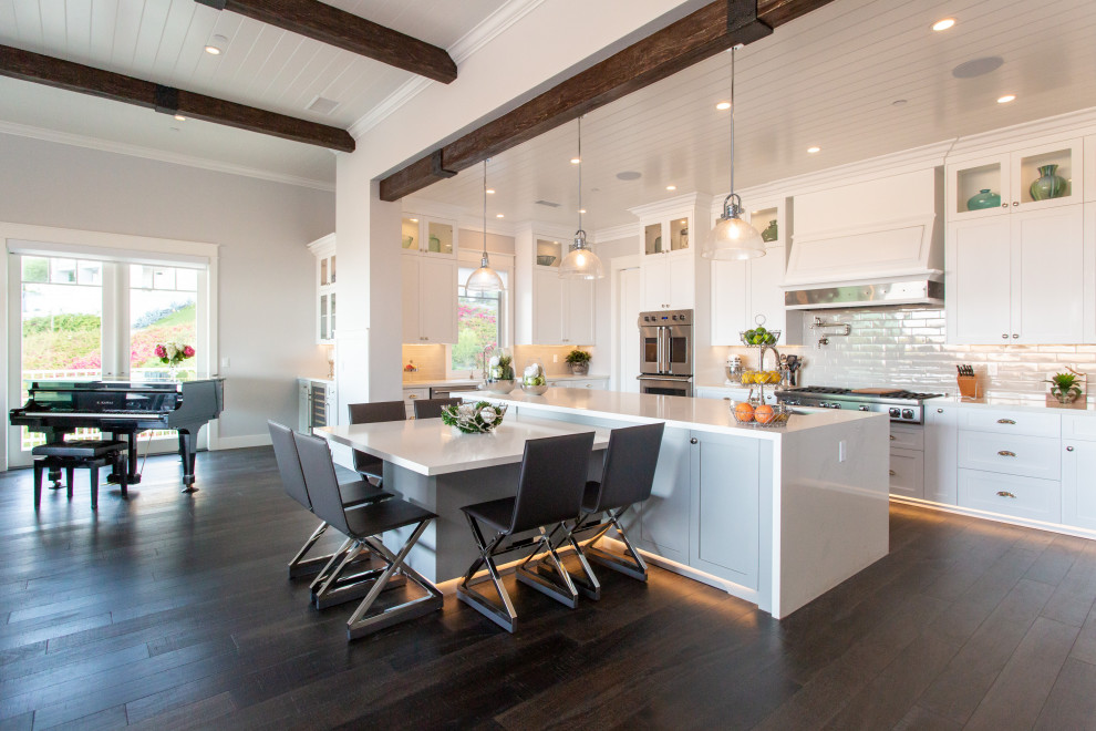 This is an example of a beach style u-shaped open plan kitchen in Orange County with an undermount sink, shaker cabinets, white cabinets, quartz benchtops, white splashback, stainless steel appliances, dark hardwood floors, with island, brown floor, white benchtop, exposed beam and timber.