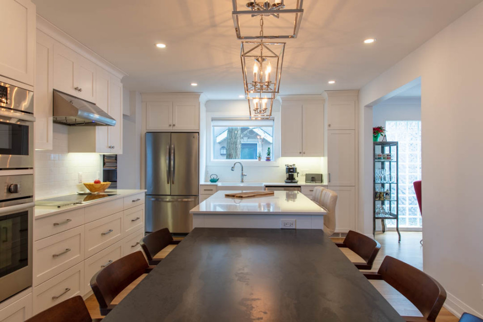 Large transitional l-shaped light wood floor eat-in kitchen photo in Ottawa with a farmhouse sink, shaker cabinets, white cabinets, quartz countertops, white backsplash, porcelain backsplash, stainless steel appliances, an island and white countertops