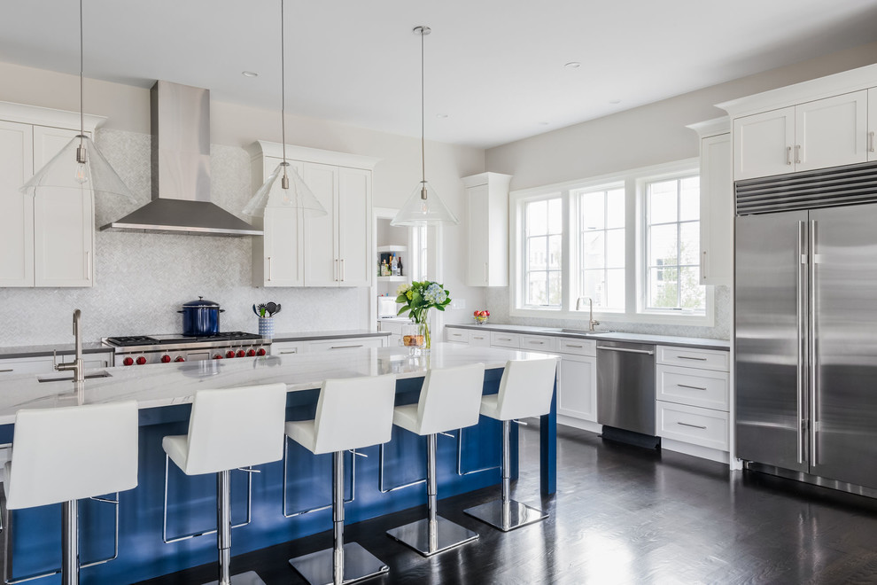 This is an example of a large transitional l-shaped open plan kitchen in Boston with an undermount sink, shaker cabinets, quartz benchtops, white splashback, marble splashback, stainless steel appliances, dark hardwood floors, with island, brown floor, white benchtop and blue cabinets.