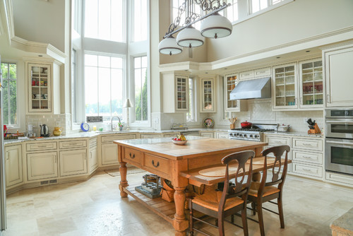 Spacious, sunlit kitchen with cream cabinets, glass-front uppers, and a rustic wood island table—Kitchen Cabinet Mississauga.