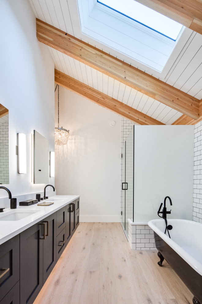 Inspiration for a mid-sized modern master bathroom in Vancouver with shaker cabinets, black cabinets, a claw-foot tub, a corner shower, a one-piece toilet, white tile, subway tile, white walls, light hardwood floors, a drop-in sink, engineered quartz benchtops, a hinged shower door, white benchtops and beige floor.