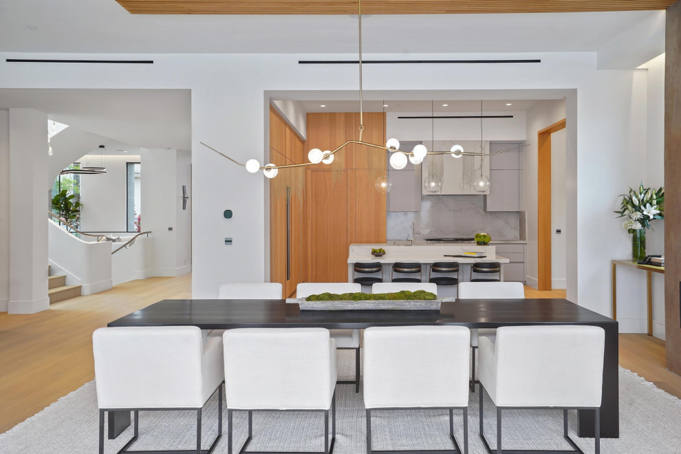 This is an example of an expansive modern u-shaped eat-in kitchen in Los Angeles with an undermount sink, flat-panel cabinets, light wood cabinets, marble benchtops, white splashback, stone slab splashback, panelled appliances, light hardwood floors, with island, brown floor, white benchtop and wood.