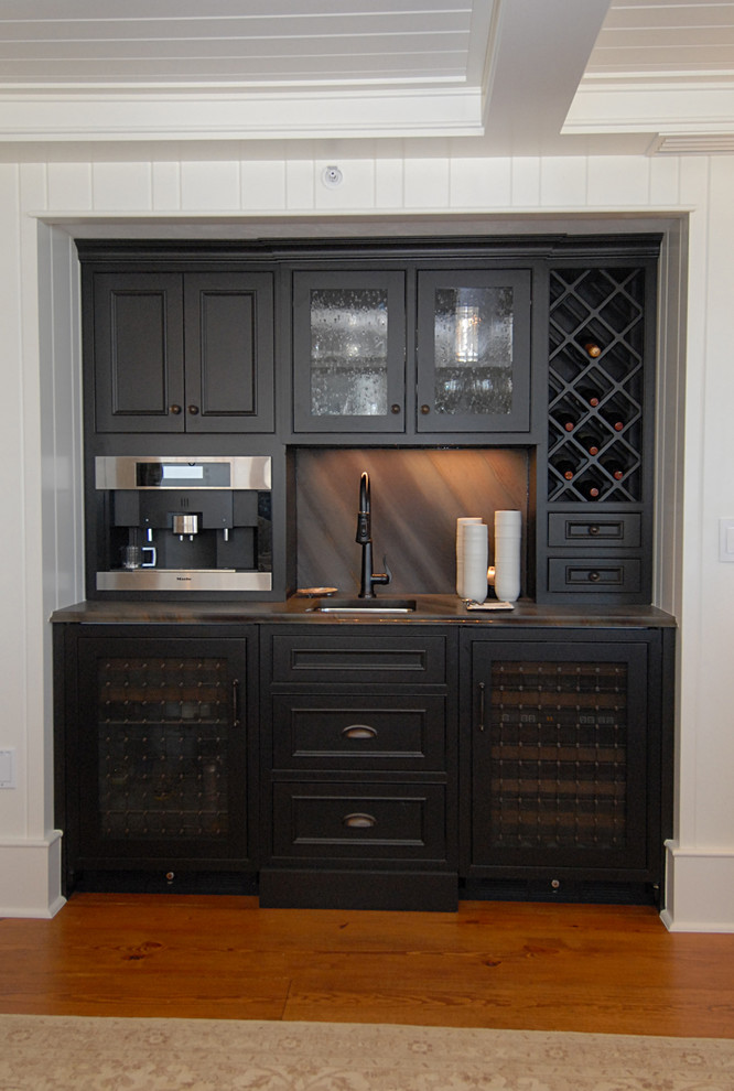 This is an example of a small beach style single-wall home bar in Orlando with an undermount sink, beaded inset cabinets, black cabinets, granite benchtops, brown splashback, stone slab splashback and medium hardwood floors.