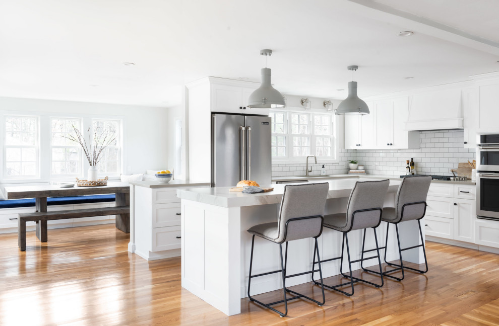 Design ideas for a mid-sized transitional u-shaped eat-in kitchen in Boston with an undermount sink, shaker cabinets, white cabinets, quartz benchtops, white splashback, subway tile splashback, stainless steel appliances, light hardwood floors, with island, beige floor and grey benchtop.