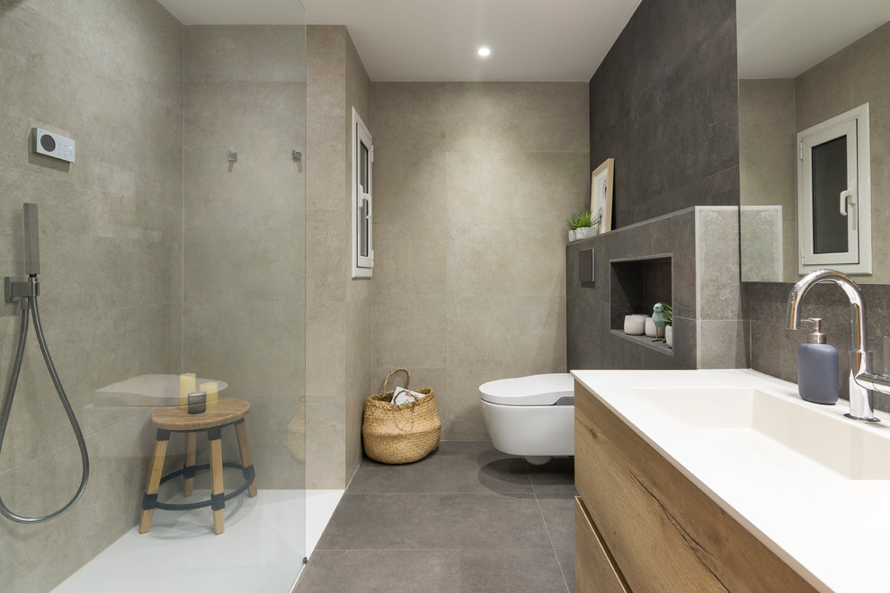 Inspiration for a scandinavian 3/4 bathroom in Barcelona with flat-panel cabinets, medium wood cabinets, a curbless shower, a wall-mount toilet, beige tile, gray tile, an integrated sink, grey floor, an open shower and white benchtops.
