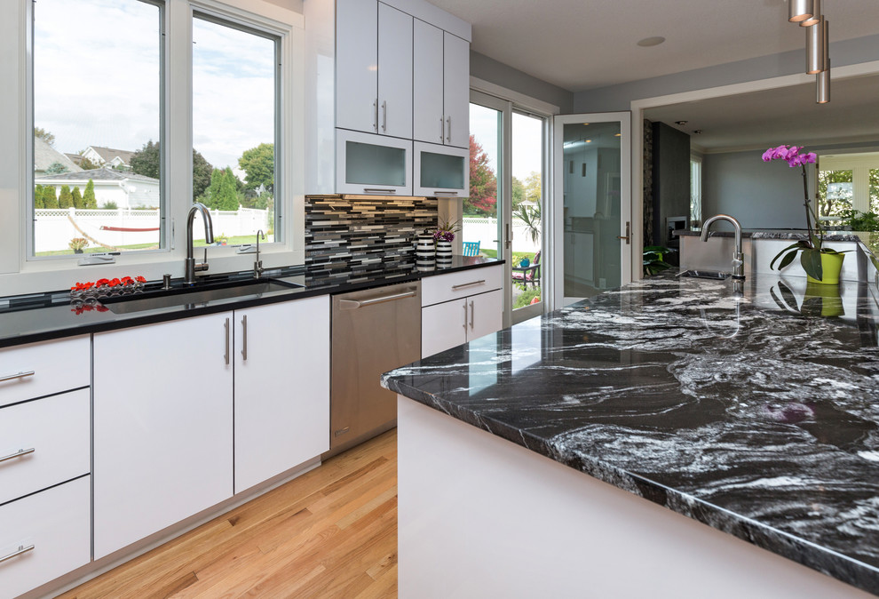 Open concept kitchen - large contemporary u-shaped light wood floor open concept kitchen idea with an undermount sink, flat-panel cabinets, white cabinets, granite countertops, multicolored backsplash, mosaic tile backsplash, stainless steel appliances and an island
