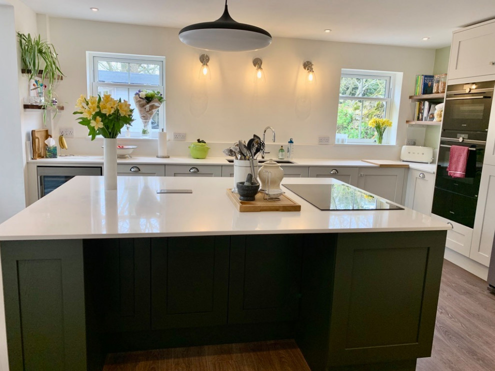 Large contemporary l-shaped kitchen/diner in Other with shaker cabinets, green cabinets, quartz worktops, white splashback, engineered quartz splashback, integrated appliances, an island, brown floors and white worktops.