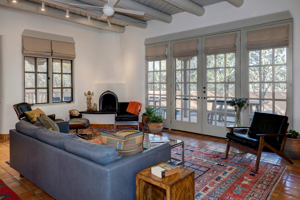 Photo of a mid-sized eclectic open concept living room in Albuquerque with white walls, terra-cotta floors, a corner fireplace, a plaster fireplace surround and orange floor.