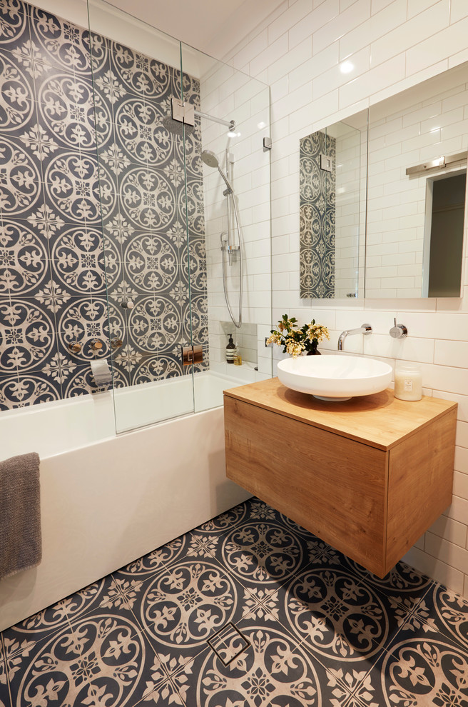 This is an example of a small contemporary master bathroom in Sydney with medium wood cabinets, a freestanding tub, a shower/bathtub combo, a wall-mount toilet, blue tile, ceramic tile, white walls, ceramic floors, a vessel sink, wood benchtops and brown benchtops.