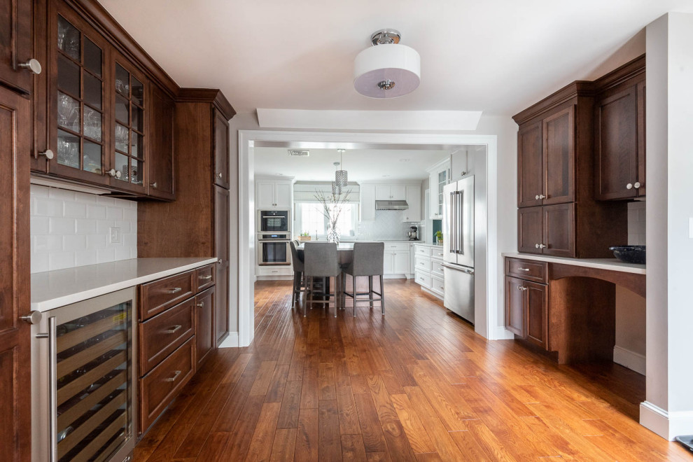 Inspiration for a large transitional l-shaped medium tone wood floor and brown floor eat-in kitchen remodel in Boston with an undermount sink, shaker cabinets, white cabinets, quartz countertops, white backsplash, subway tile backsplash, stainless steel appliances, an island and white countertops