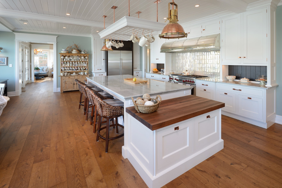 This is an example of a country u-shaped kitchen in Chicago with stainless steel appliances, medium hardwood floors, with island, beaded inset cabinets, yellow cabinets, quartzite benchtops and white splashback.