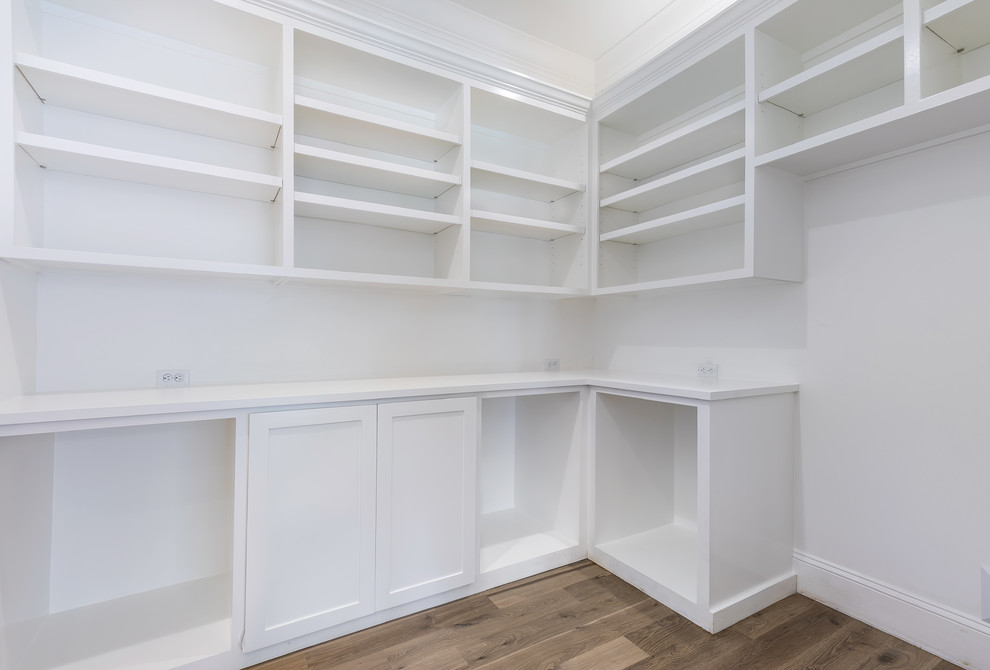 This is an example of a mid-sized traditional gender-neutral walk-in wardrobe in Jacksonville with shaker cabinets, white cabinets, medium hardwood floors and brown floor.
