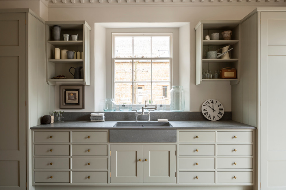 This is an example of a mid-sized country galley laundry room in Gloucestershire with recessed-panel cabinets, limestone benchtops, white walls, limestone floors, grey cabinets and a single-bowl sink.