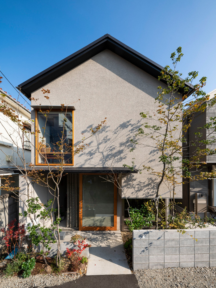 Aménagement d'une petite façade de maison beige classique en stuc à un étage avec un toit à deux pans, un toit en métal et un toit noir.