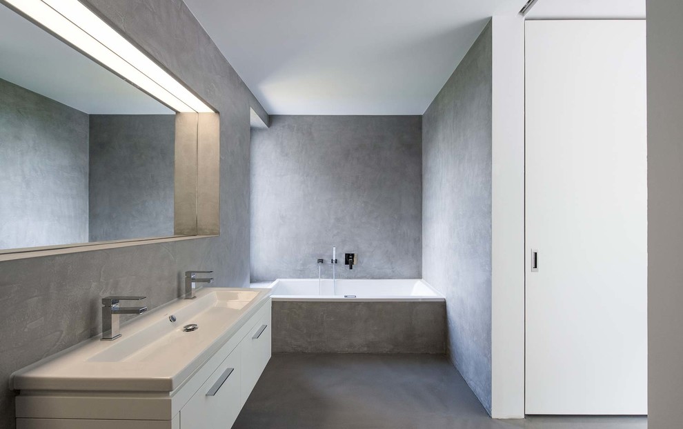 This is an example of a mid-sized modern master bathroom in Other with flat-panel cabinets, white cabinets, a drop-in tub, gray tile, grey walls, concrete floors, a vessel sink and solid surface benchtops.