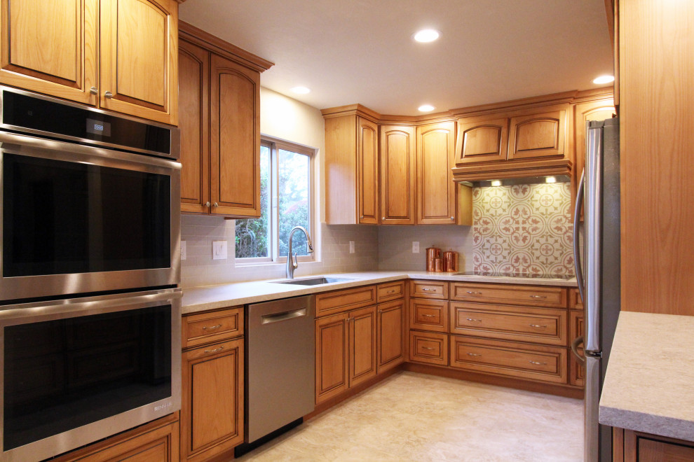 Mid-sized u-shaped porcelain tile and beige floor eat-in kitchen photo with an undermount sink, raised-panel cabinets, medium tone wood cabinets, quartz countertops, multicolored backsplash, ceramic backsplash, stainless steel appliances, a peninsula and multicolored countertops
