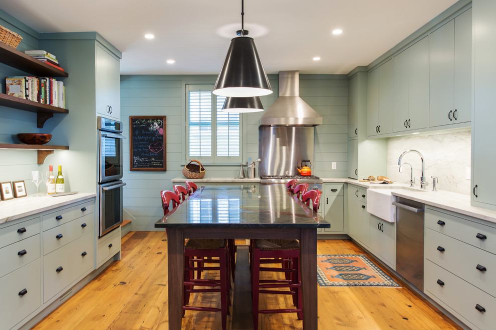 Large country kitchen in New York with a farmhouse sink, flat-panel cabinets, stainless steel appliances, medium hardwood floors, with island, green cabinets, white splashback, marble splashback and orange floor.
