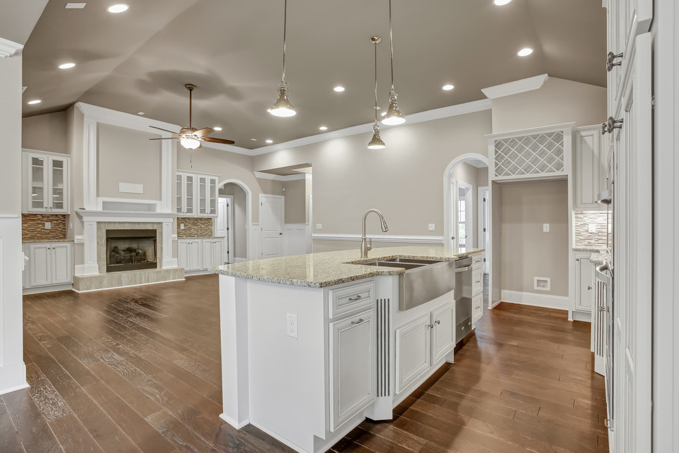 Mid-sized transitional l-shaped dark wood floor open concept kitchen photo with a farmhouse sink, recessed-panel cabinets, white cabinets, granite countertops, beige backsplash, mosaic tile backsplash, stainless steel appliances and an island