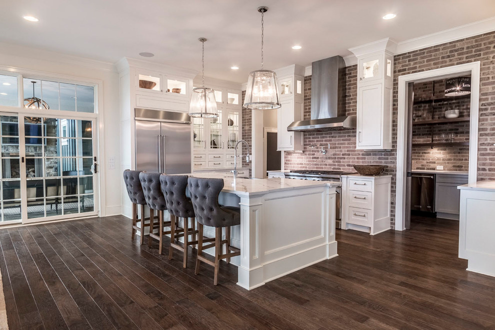 Inspiration for a large transitional l-shaped kitchen in Columbus with an undermount sink, recessed-panel cabinets, white cabinets, quartz benchtops, brown splashback, brick splashback, stainless steel appliances, medium hardwood floors, with island and brown floor.