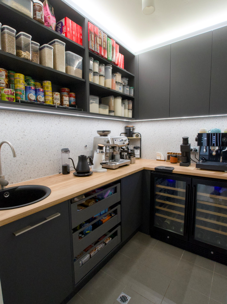 Inspiration for a small contemporary l-shaped kitchen pantry in Adelaide with a drop-in sink, wood benchtops, white splashback, porcelain splashback, black appliances, porcelain floors and grey floor.