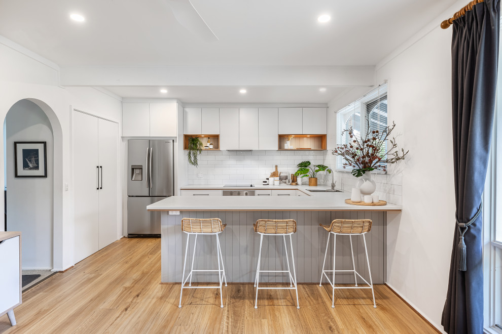 Inspiration for a mid-sized contemporary u-shaped eat-in kitchen in Adelaide with a single-bowl sink, white cabinets, laminate benchtops, white splashback, subway tile splashback, stainless steel appliances, medium hardwood floors, a peninsula, brown floor and white benchtop.
