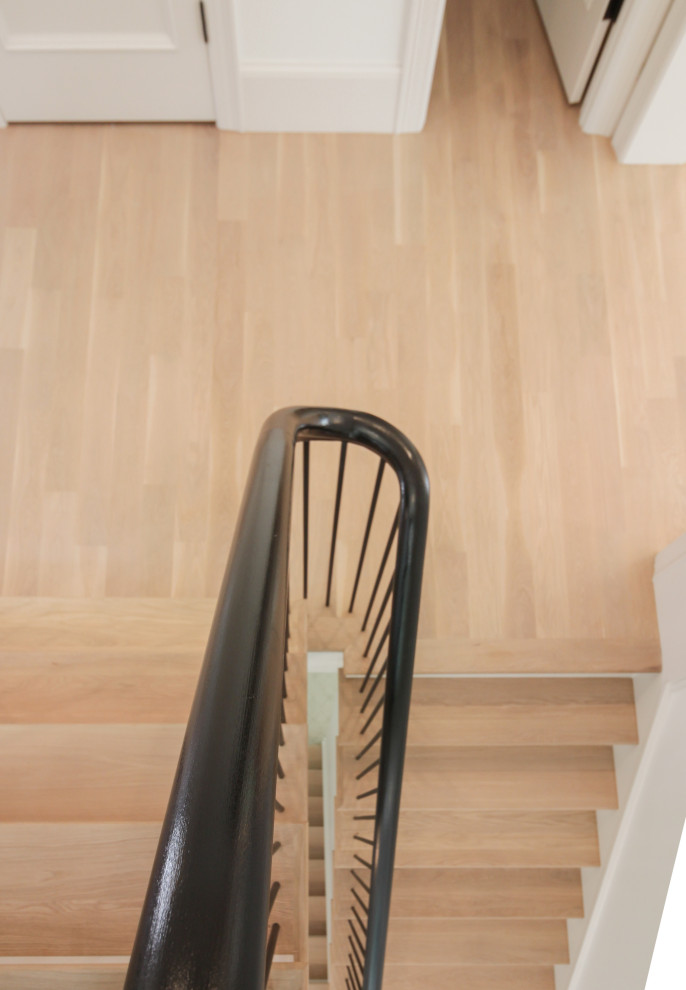 На фото: большая п-образная лестница в стиле модернизм с деревянными ступенями, крашенными деревянными подступенками, перилами из смешанных материалов и панелями на стенах