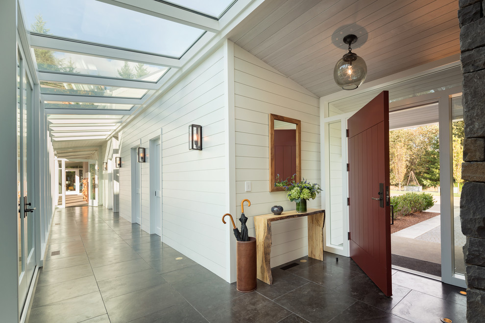 Example of a large trendy slate floor and black floor entry hall design with white walls and a red front door