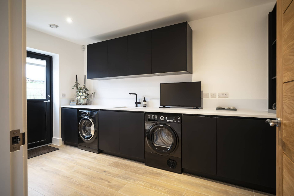 Photo of a large modern single-wall open plan kitchen in Oxfordshire with a drop-in sink, flat-panel cabinets, black cabinets, quartzite benchtops, white splashback, with island and white benchtop.