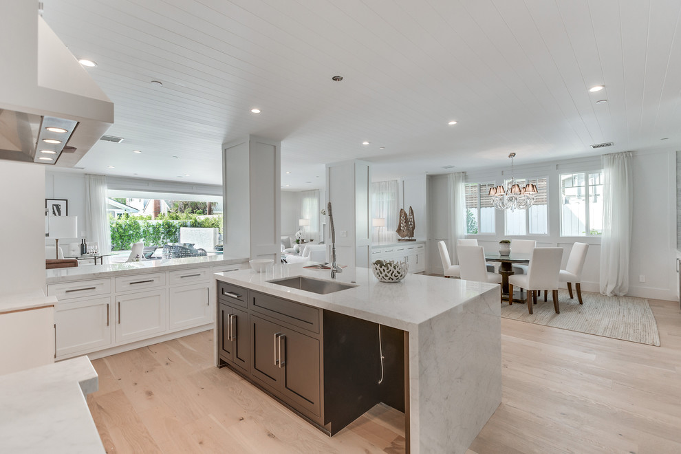 This is an example of a large contemporary u-shaped eat-in kitchen in Los Angeles with a drop-in sink, shaker cabinets, white cabinets, marble benchtops, white splashback, ceramic splashback, light hardwood floors, with island and brown floor.