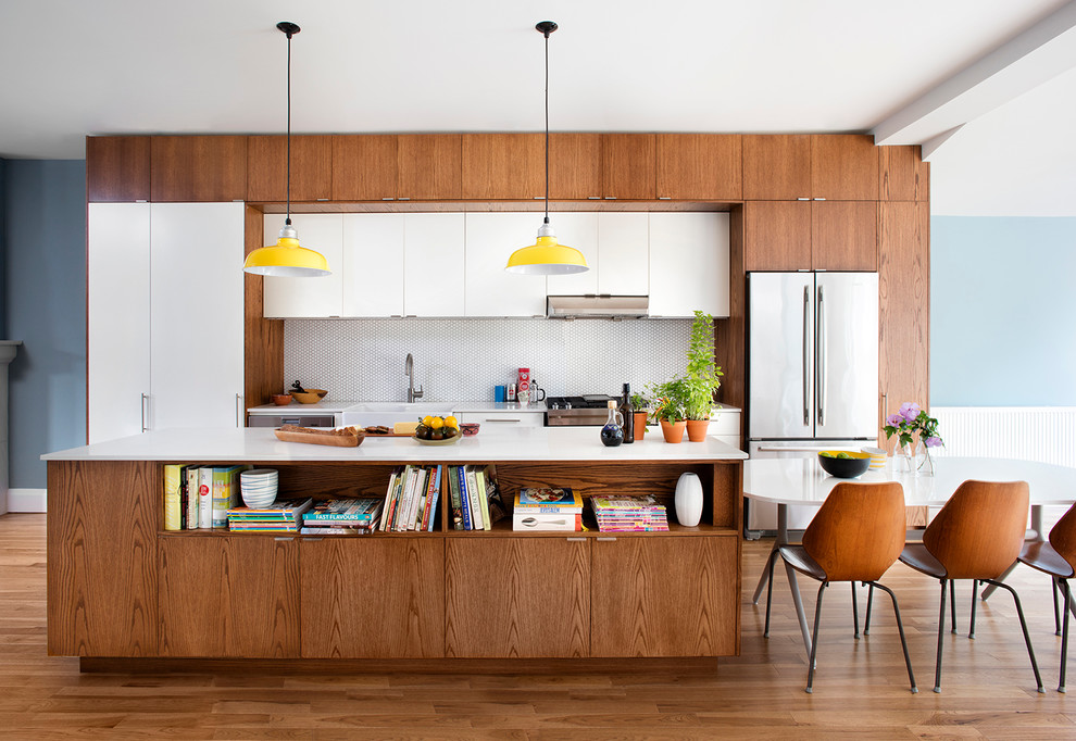 This is an example of a midcentury single-wall eat-in kitchen in Toronto with a farmhouse sink, flat-panel cabinets, medium wood cabinets, white splashback, mosaic tile splashback, stainless steel appliances and with island.