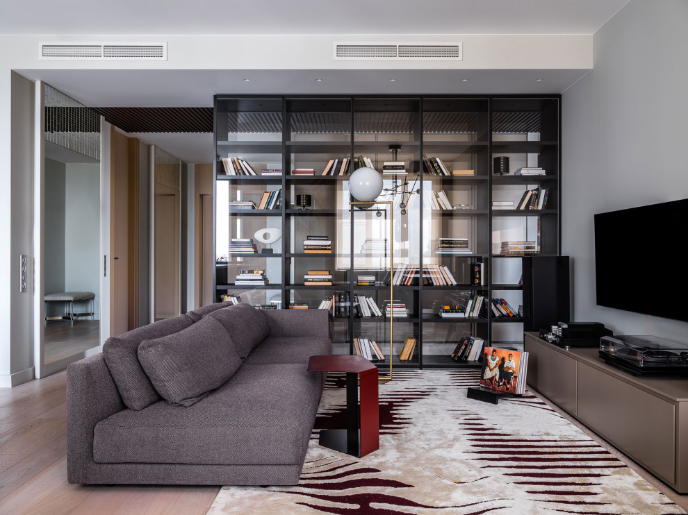 Esempio di un grande soggiorno design aperto con libreria, pareti beige, pavimento in legno massello medio, TV a parete e pavimento beige