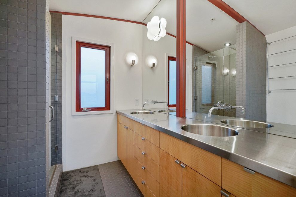 Design ideas for a mid-sized eclectic master bathroom in San Francisco with flat-panel cabinets, medium wood cabinets, an alcove shower, a one-piece toilet, gray tile, ceramic tile, white walls, ceramic floors, an integrated sink, stainless steel benchtops, grey floor, a hinged shower door and grey benchtops.