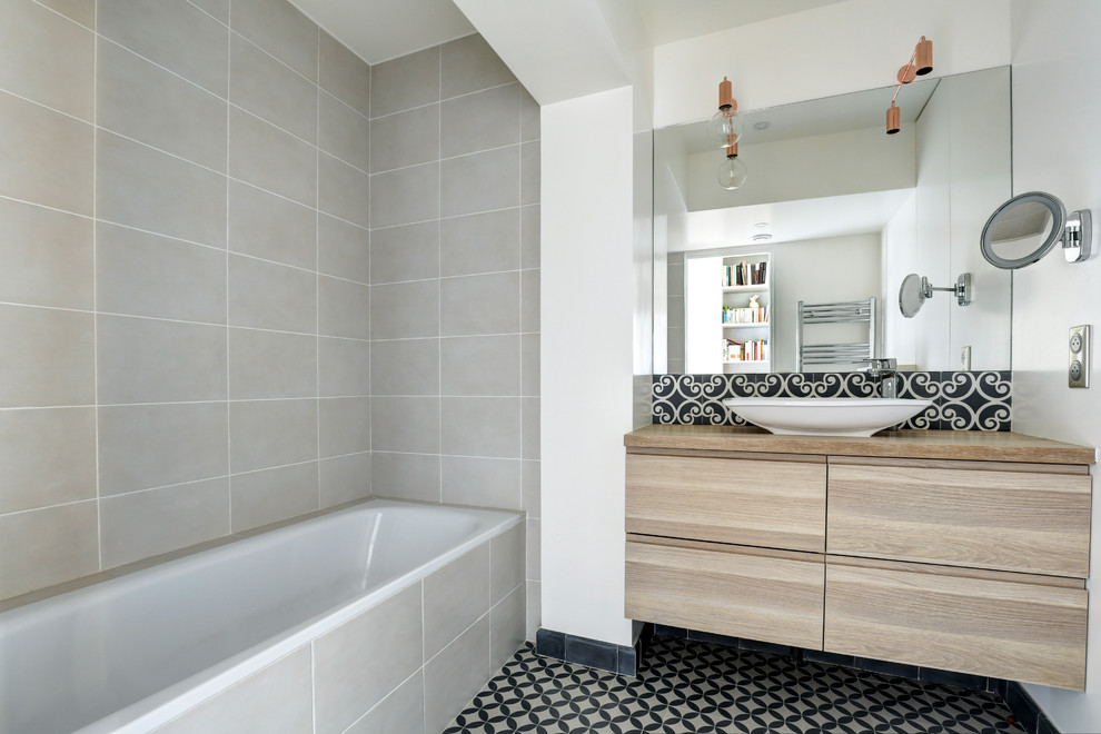 Photo of a scandinavian 3/4 bathroom in Tel Aviv with flat-panel cabinets, medium wood cabinets, a drop-in tub, gray tile, white walls, a vessel sink, wood benchtops, multi-coloured floor and brown benchtops.