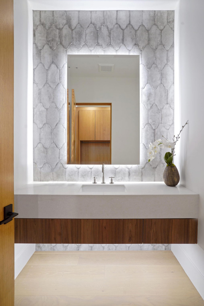 Bild på ett litet funkis vit vitt toalett, med släta luckor, skåp i mellenmörkt trä, grå kakel, keramikplattor, vita väggar, ljust trägolv, ett undermonterad handfat, bänkskiva i akrylsten och brunt golv