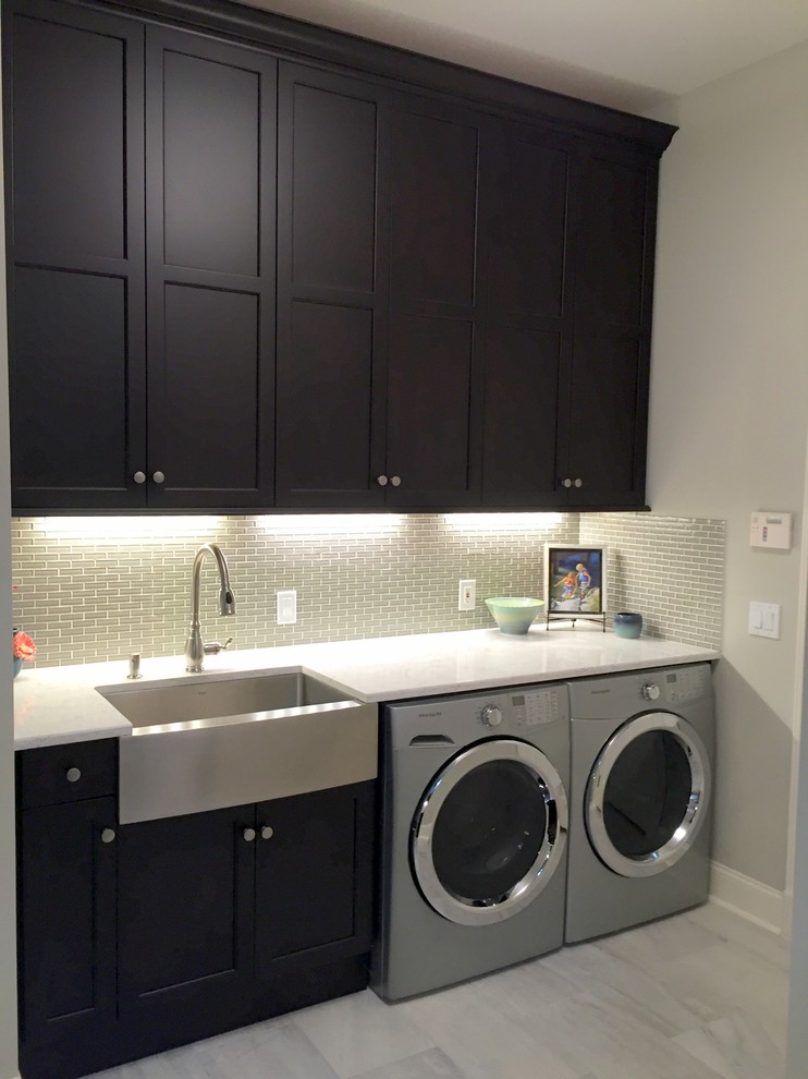 Inspiration for a mid-sized transitional l-shaped utility room in Charleston with a farmhouse sink, recessed-panel cabinets, dark wood cabinets, quartz benchtops, grey walls, porcelain floors and a side-by-side washer and dryer.