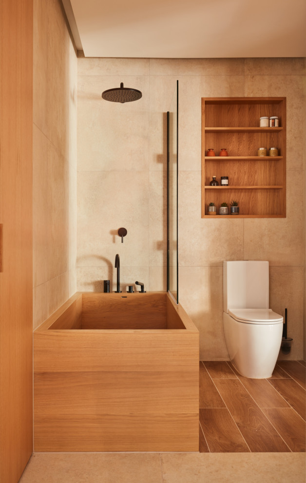 This is an example of a medium sized modern ensuite bathroom in London with flat-panel cabinets, black cabinets, a japanese bath, a shower/bath combination, a one-piece toilet, beige tiles, porcelain tiles, beige walls, porcelain flooring, a wall-mounted sink, beige floors, a wall niche, a single sink and a floating vanity unit.