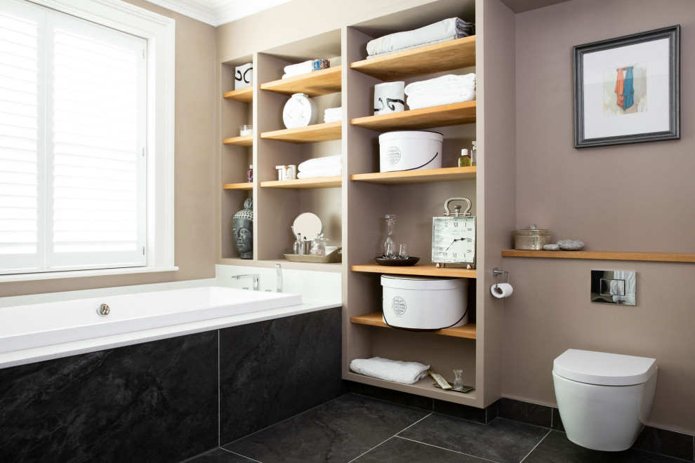 Cette image montre une salle d'eau traditionnelle avec une baignoire posée, WC à poser, un mur marron et un sol noir.
