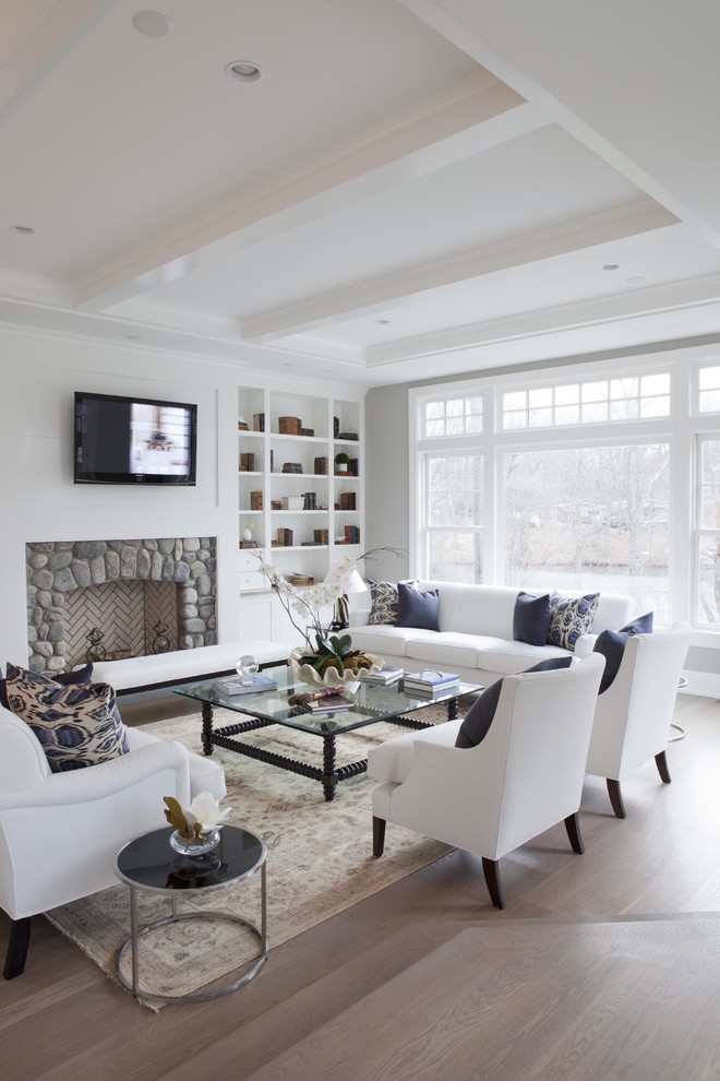Photo of a transitional family room in New York with white walls, light hardwood floors, a standard fireplace, a stone fireplace surround and a wall-mounted tv.