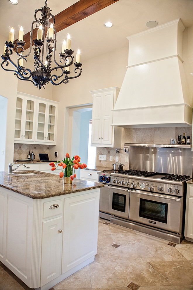 Example of a large classic travertine floor kitchen design in Austin with a farmhouse sink, recessed-panel cabinets, white cabinets, granite countertops, travertine backsplash, stainless steel appliances and an island