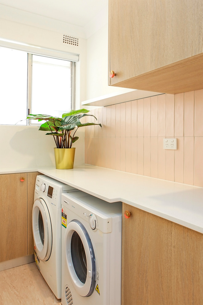 Photo of a small single-wall dedicated laundry room in Sydney with flat-panel cabinets, light wood cabinets, quartz benchtops, pink splashback, ceramic splashback, yellow walls, vinyl floors, a side-by-side washer and dryer, pink floor and white benchtop.