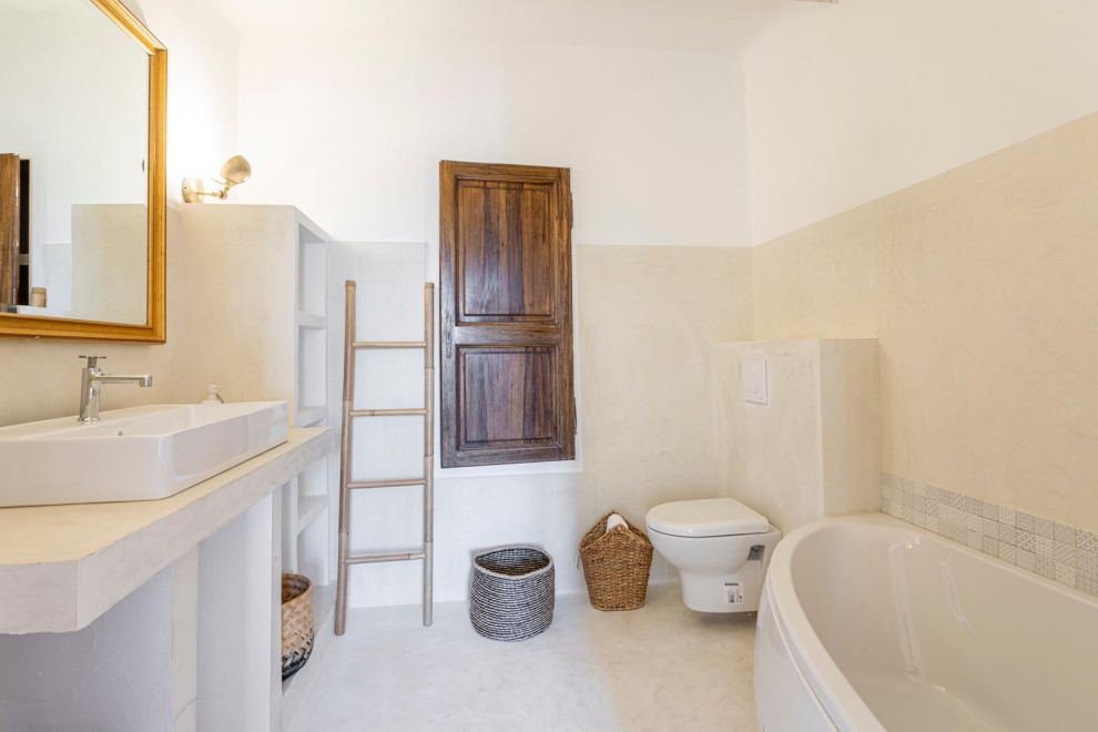 This is an example of a mid-sized beach style bathroom in Other with open cabinets, an alcove tub, a wall-mount toilet, beige walls, terra-cotta floors, a drop-in sink, beige floor and beige benchtops.