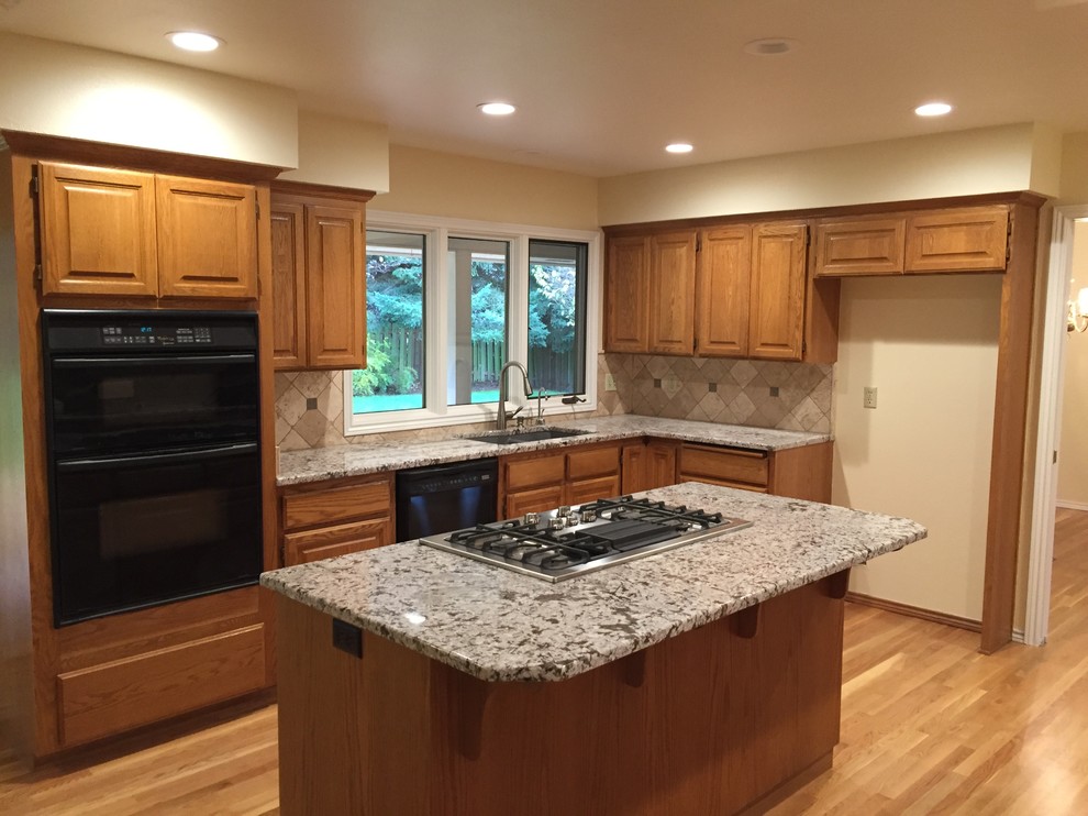 This is an example of a mid-sized traditional u-shaped eat-in kitchen in Portland with an undermount sink, raised-panel cabinets, medium wood cabinets, granite benchtops, beige splashback, stone tile splashback, black appliances, medium hardwood floors and with island.