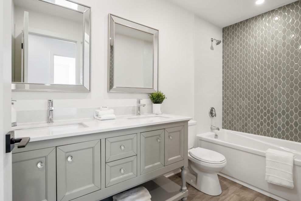 This is an example of a mid-sized country kids bathroom in Montreal with furniture-like cabinets, grey cabinets, a shower/bathtub combo, a two-piece toilet, gray tile, pebble tile, white walls, porcelain floors, an undermount sink, engineered quartz benchtops, brown floor, a shower curtain, white benchtops, a double vanity and a built-in vanity.