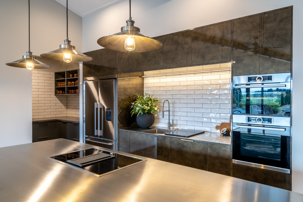 Inspiration for a mid-sized industrial galley kitchen pantry in Other with a single-bowl sink, flat-panel cabinets, grey cabinets, stainless steel benchtops, white splashback, subway tile splashback, stainless steel appliances, vinyl floors, with island and brown floor.