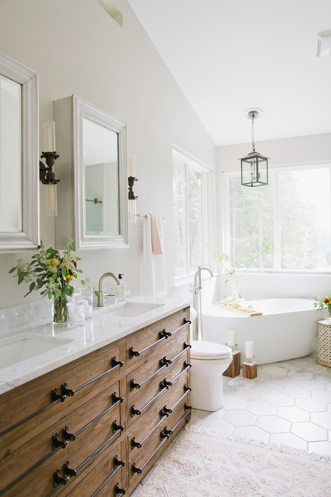 Inspiration for a mid-sized transitional master bathroom in Seattle with furniture-like cabinets, distressed cabinets, a freestanding tub, an alcove shower, a two-piece toilet, gray tile, porcelain tile, grey walls, porcelain floors, an undermount sink, marble benchtops, grey floor, a sliding shower screen and white benchtops.