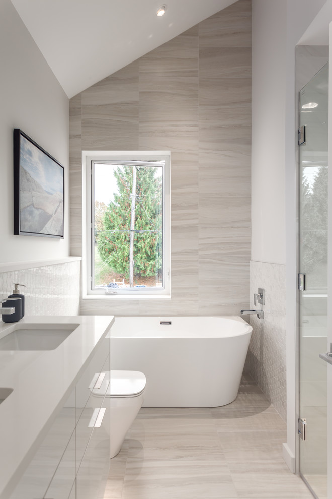 Photo of a mid-sized modern master wet room bathroom in Vancouver with furniture-like cabinets, white cabinets, a freestanding tub, ceramic tile, quartzite benchtops, a hinged shower door, a one-piece toilet, beige tile, grey walls, porcelain floors, an undermount sink, beige floor and white benchtops.