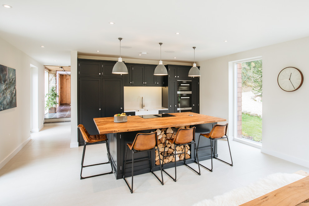 This is an example of a transitional single-wall kitchen in Other with shaker cabinets, black cabinets, wood benchtops, white splashback, black appliances, with island, white floor and brown benchtop.