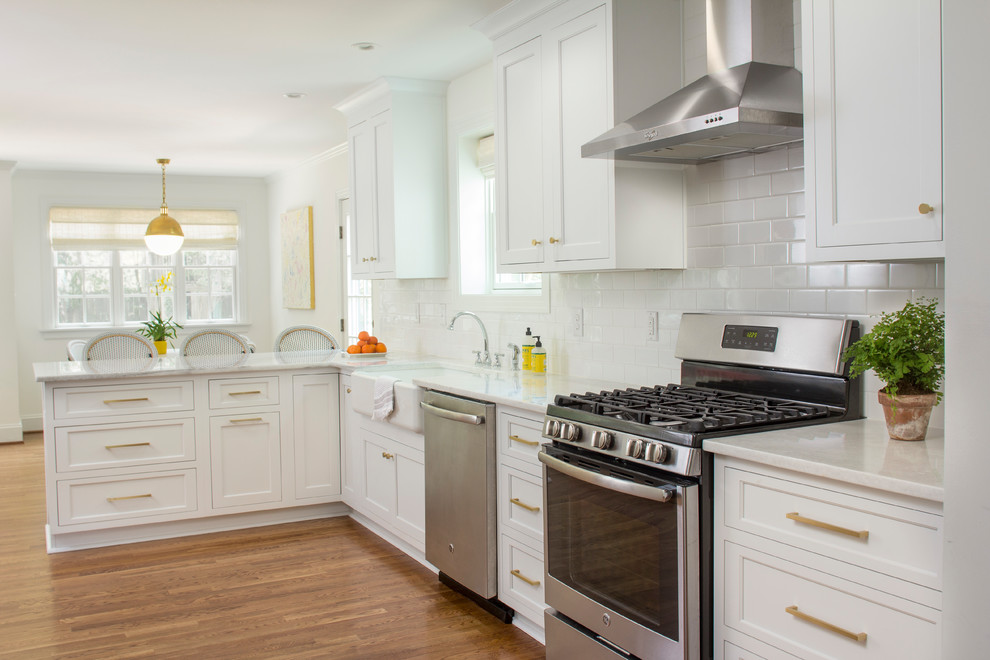 Open concept kitchen - transitional l-shaped medium tone wood floor and brown floor open concept kitchen idea with a farmhouse sink, shaker cabinets, white cabinets, marble countertops, white backsplash, ceramic backsplash, stainless steel appliances and a peninsula
