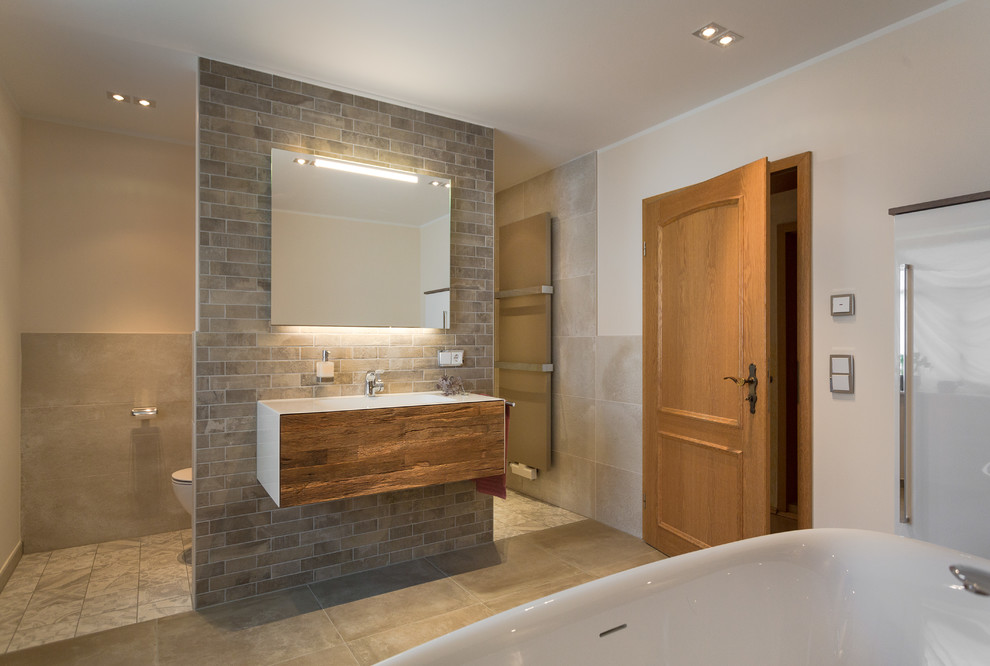 Badezimmer En Suite With flächenbündigen Schrankfronten, hellbraunen Holzschränken, freistehender Badewanne, offener Dusche, beigen Fliesen, beiger Wandfarbe, integriertem Waschbecken and beigem Boden in Dresden