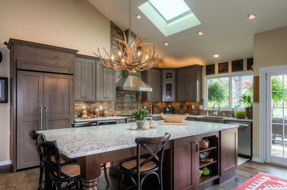 Large mountain style l-shaped dark wood floor and brown floor eat-in kitchen photo in Denver with a farmhouse sink, shaker cabinets, dark wood cabinets, quartzite countertops, brown backsplash, stone tile backsplash, paneled appliances and an island